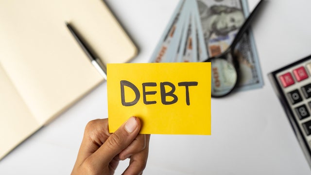 Hands Holding "DEBT" Label with Financial Tools and Money 