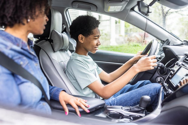 Mother teaching teenage son how to drive in front seat of car 