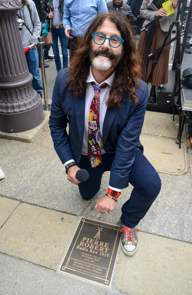 WMMR's Pierre Robert kneels behind his plaque it on the Philadelphia Music Alliance Walk of Fame at University of the Arts