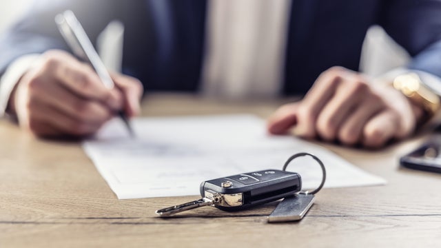 The agent signs a contract for the purchase or Leasing of a new car. New car keys in the foreground. 