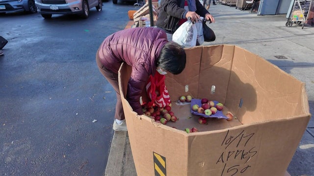 An individual reaches into a nearly-empty bin of apples at a food bank. 