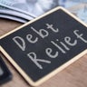 A blackboard with Debt Relief written in chalk, a calculator and US dollar bills. 