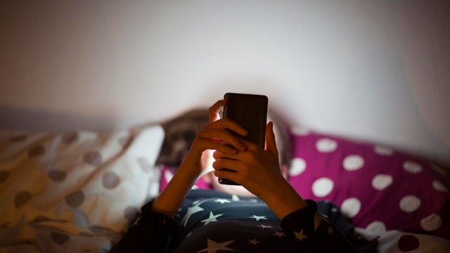 Girl lying on bed at night and using a mobile phone 
