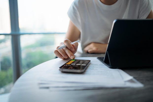 Asian woman managing personal banking and finance. Paying bills online. Making financial plans. Planning budget and calculating expenses with digital tablet while going through bills at home. Home finances. Home budgeting. Banking and finance concept 