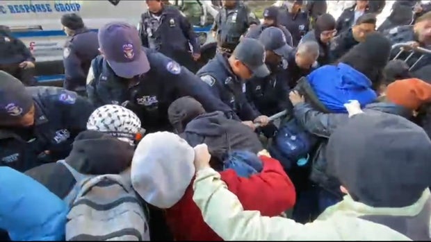 Protesters and NYPD officers on opposite sides of a metal barricade