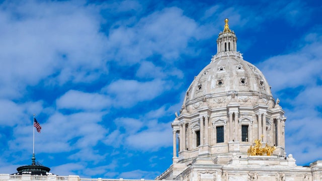 Minnesota state capitol with American flag and blue sky with clouds. 