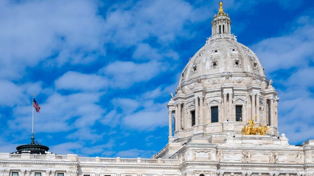 Minnesota state capitol with American flag and blue sky with clouds. 