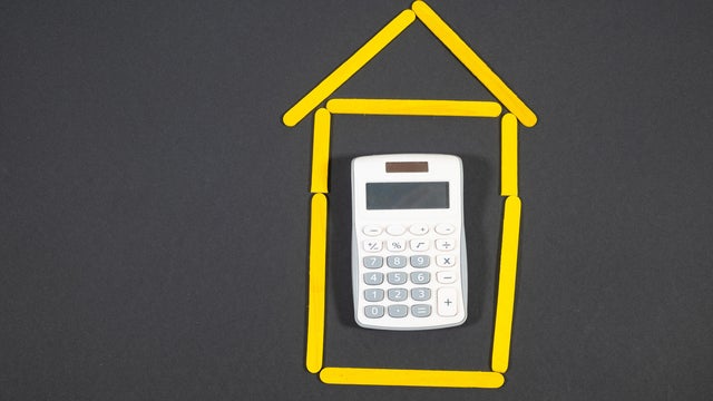 Concept of buying a house: a c calculator inside a drawing of a house made of yellow sticks. 