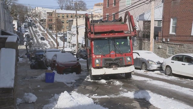 A red trash truck navigates an icy, hilly street in Manayunk 