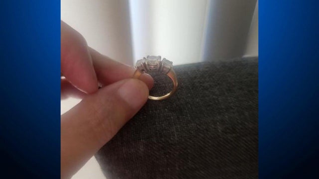 A diamond wedding ring being pinched between a thumb and middle finger 