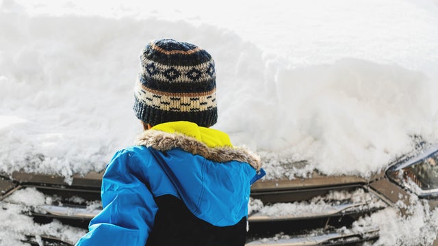A boy wearing a winter coat and hat Clears Snow From a Car 
