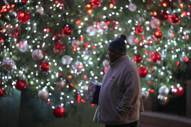 Ahmad Collins, is seen holding a gift, walking in front of a lit Christmas tree in Harrisburg