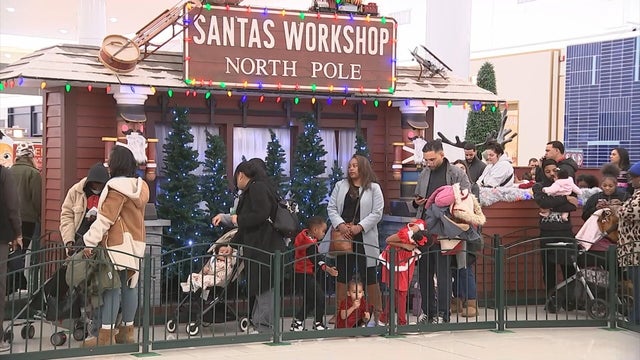 People line up in front of a sign that says Santa's Workshop North Pole at the Cherry Hill Mall 