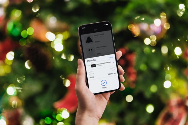Female hand doing Christmas shopping online with smartphone, making mobile payment with credit card against illuminated Christmas tree with fairy lights. Christmas theme. Christmas shopping. Christmas sale. Contactless payment. Lifestyle and technology 