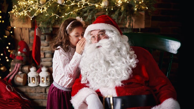 Young girl visiting Santa, whispering into Santas ear 