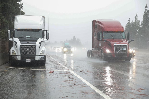 A person in a safety vest standing in water as he rakes leaves 