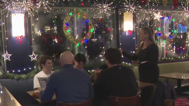 A group of people sit at a table while a waitress talks to them 