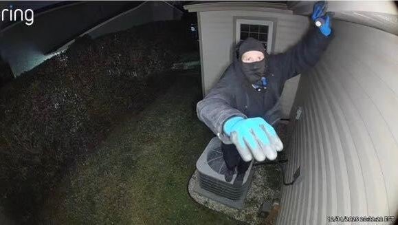 A man is seen reaching toward the camera, wearing blue gloves and holding a screwdriver