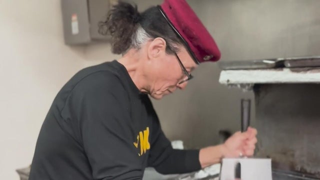 A man with a red hat holds spatulas near a grill 