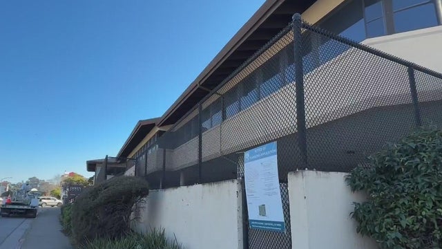 A vacant office building sits behind a chain-link fence 