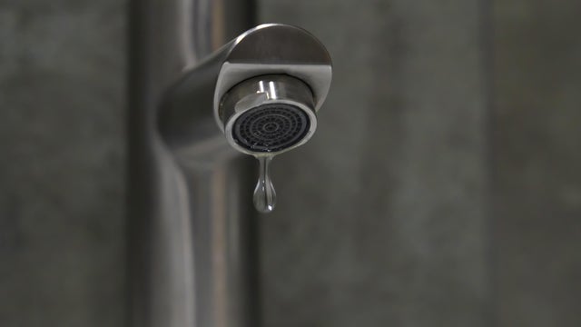 Close-up of a dripping faucet with a single drop of water forming, highlighting the importance of water conservation and the need to fix leaks to prevent water waste 