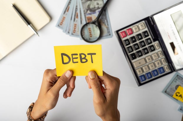 Hands Holding "DEBT" Label with Financial Tools and Money 