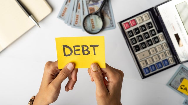 Hands Holding "DEBT" Label with Financial Tools and Money 