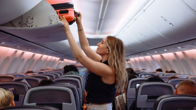 Woman putting hand baggage in lockers above seats of plane 