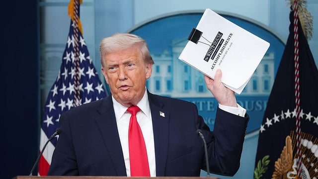 President Trump displays a stack of papers labeled "The White House Accomplishments" in the James S. Brady Press Briefing Room at the White House in Washington, D.C., on Jan. 20, 2026. 