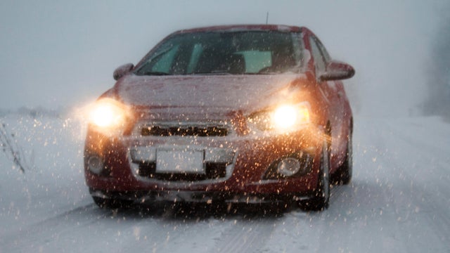 Car with headlights on driving along foggy snow covered road 