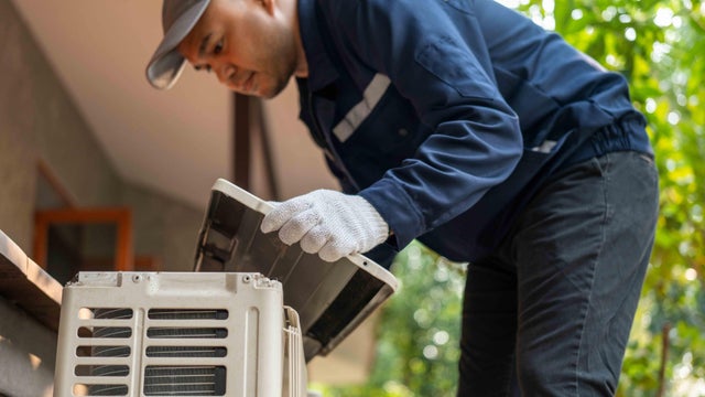 Air conditioner service outdoor checking fix repair. Air conditioner cleaning technician He opened the front cover and took out the filters and washed it. He in uniform wearing rubber 