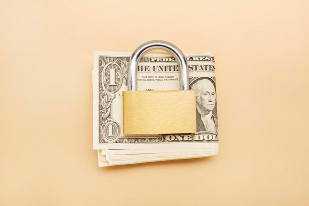 High angle view of a bunch of American Dollar banknotes and closed padlock on beige background 
