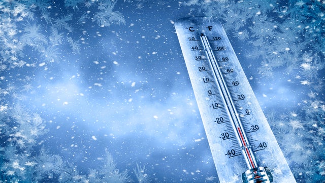 Outdoor thermometer indicating a very cold temperature. The scene is wintry, featuring falling snow and icy, frosty textures around the edges. 