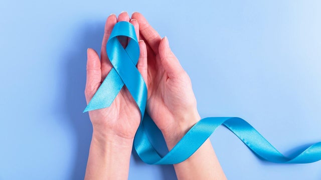 Colorectal cancer ribbon in female hands on blue background 