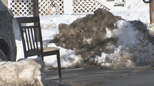 An adult man holds a shovel with a large pile of freshly fallen snow in the middle of a snowfall. 