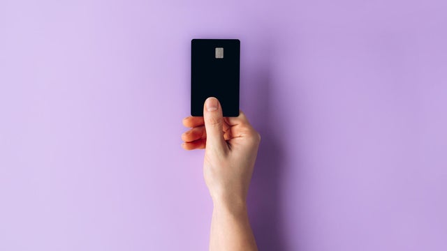 Female hand holding a black credit card against a pastel purple background for payment or finance concept 