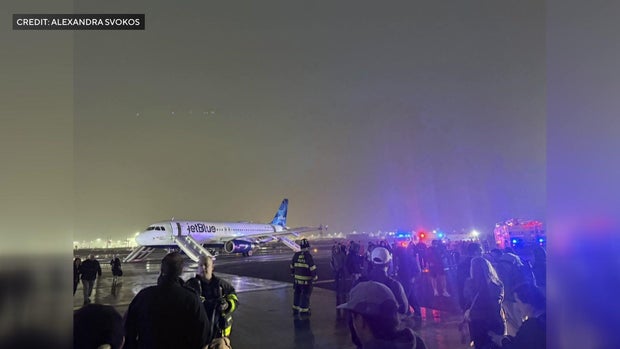 A JetBlue plane on the taxiway with its emergency slides deployed and passengers on the tarmac. 