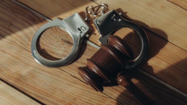 Gavel and cuffs in sunlight on a wood surface. 