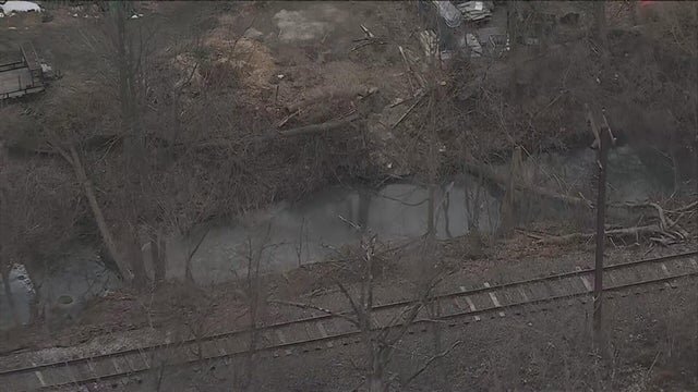 Overhead photo of the creek, which is next to railroad tracks, some of the water looks milky, some foam is seen 
