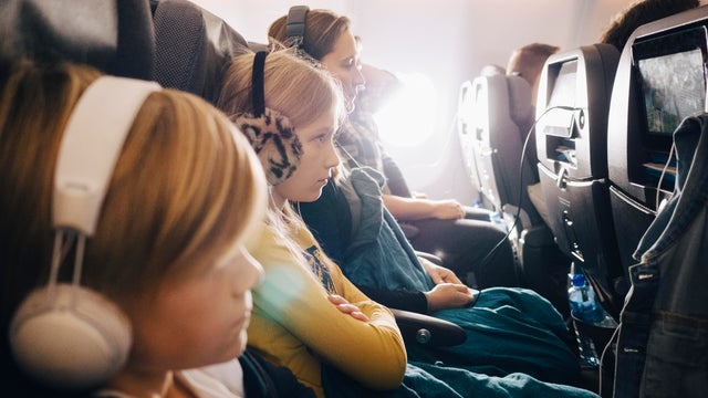 Side view of mother and children sitting in airplane while using headphones 