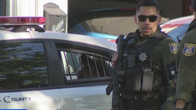 a sheriff's deputy stands in front of a patrol vehicle 