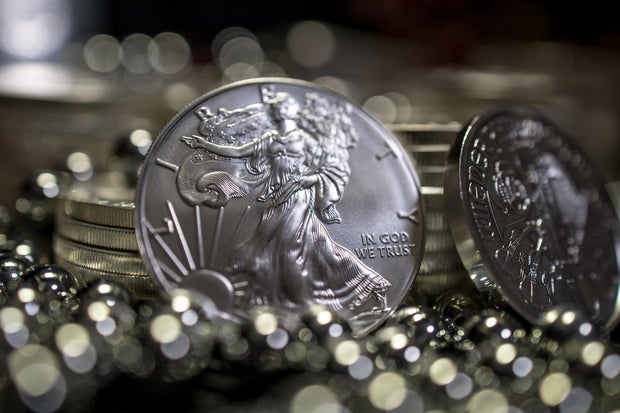 Close up of the American Liberty Silver coin among piles of silver ball bearings against a dark background 