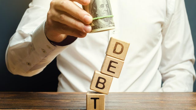 Businessman removes wooden blocks with the word Debt. Debt relief or cancellation is the partial or total forgiveness of debts, or the slowing or stopping growth. Restructuring. Pay. Selective focus 