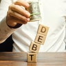 Businessman removes wooden blocks with the word Debt. Debt relief or cancellation is the partial or total forgiveness of debts, or the slowing or stopping growth. Restructuring. Pay. Selective focus 