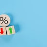 Percentage icon on wooden cube block and up and down arrow symbol on flipping white dice on blue background 