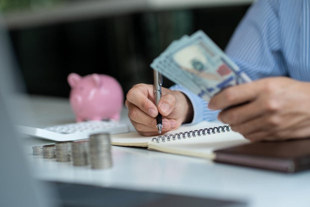 man holding a dollar bill use money calculator Keep a record of the amount of money he accumulates throughout the year with piles of coins and piggy banks for future business investments. 