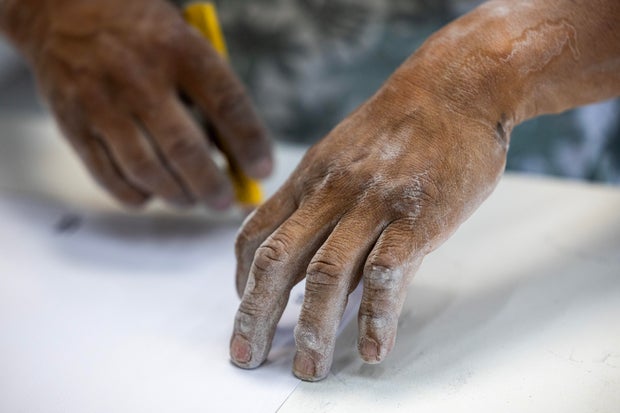 stone countertop fabricator's hands are covered in dust 