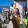 Woman contemplating rising gas prices and environmental impact while refueling car on sunny day. The intersection of transportation, energy, and the environment in everyday life 