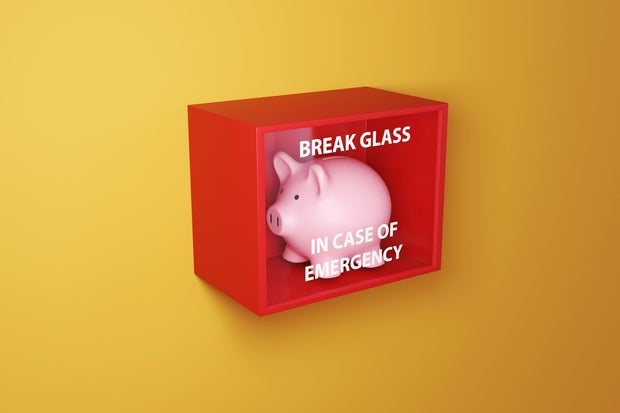 Pink piggy bank in a red box with a glass printed with the instruction BREAK GLASS IN CASE OF EMERGENCY on a yellow wall. Illustration of the concept of emergency fund and financial buffer 