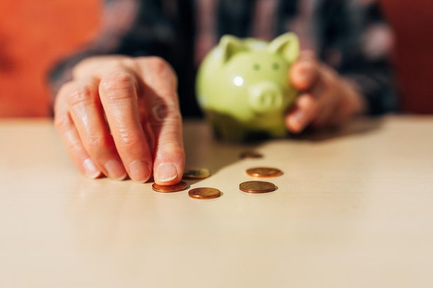 senior women Hand collecting coins on a table with a piggy bank in the background